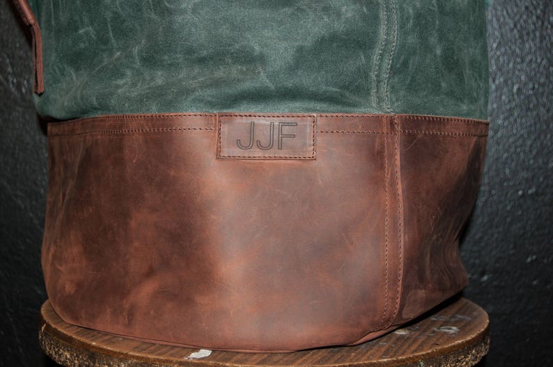 May include: A brown leather tote bag with a green canvas top. The bag has a leather strap and a personalized label that reads "JJF".