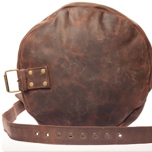 May include: A brown leather duffel bag with a brass buckle and rivets. The bag has a strap with multiple eyelets.