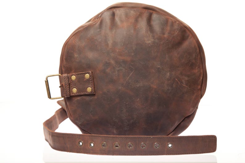 May include: A brown leather duffel bag with a brass buckle and rivets. The bag has a strap with multiple eyelets.