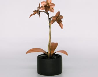 May include: A copper orchid sculpture with two flowers and leaves in a black pot. The sculpture is on a white background.