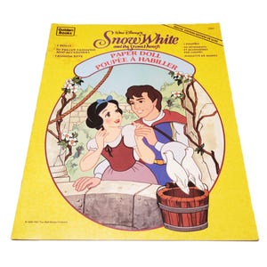 May include: A vintage Golden Books Snow White and the Seven Dwarfs paper doll set. The cover features an illustration of Snow White and the Prince, with doves and a wooden bucket. The text includes "Paper Doll" and "Deluxe Edition".