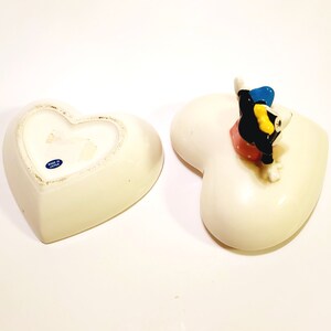 May include: White ceramic heart-shaped trinket box with a cartoon character figurine on top. The figurine is black and white with yellow and blue accents. The box is made in Japan.