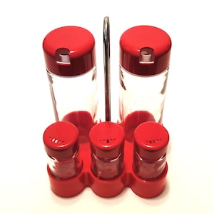 May include: A red and clear glass spice rack set. The set includes two tall spice jars with red lids and three smaller spice jars with red shaker lids. A silver metal handle is attached to the red base.