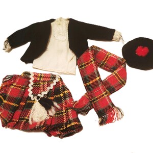 May include: A miniature Scottish outfit, featuring a black jacket, white shirt, red and black plaid kilt, scarf, and a black hat with a red pom-pom. The kilt has a white lace trim and a black and white tassel.