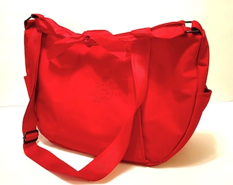 May include: A bright red shoulder bag with a long strap and a bow detail. The bag has a small pocket on the front and a larger pocket on the back.
