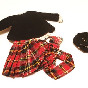 May include: A doll-sized school uniform set, featuring a black velvet jacket with lace trim, a red plaid pleated skirt, a matching tie, and a black hat with white embroidery. The set is designed for a doll.