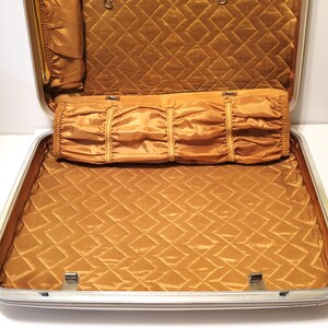 May include: Open vintage suitcase with a silver frame and a gold quilted interior. The interior features a diamond pattern and several compartments, including a roll-up section. The suitcase is empty and ready for travel.