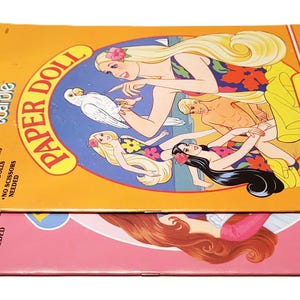 Pode incluir: Dois conjuntos de bonecas de papel Barbie vintage. O conjunto superior apresenta um tema tropical com ilustra&ccedil;&otilde;es da Barbie e amigos, um papagaio e as palavras "PAPER DOLL". O conjunto inferior &eacute; rosa com uma ilustra&ccedil;&atilde;o da Barbie.