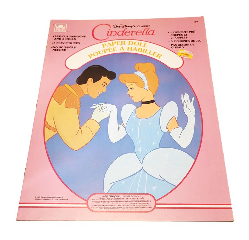 Pode incluir: Um livro de bonecas de papel vintage da Cinderela com uma capa rosa. A capa apresenta ilustra&ccedil;&otilde;es da Cinderela e do Pr&iacute;ncipe Encantado. O texto inclui "Modas pr&eacute;-cortadas e 2 bonecas" e "Sem necessidade de tesoura".