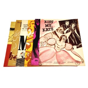 May include: A stack of vintage theatre programmes, with colourful illustrations and the title "Kiss Me, Kate." The programmes feature various designs, including images of performers and the text "Theatre Under The Stars, Vancouver, B.C."
