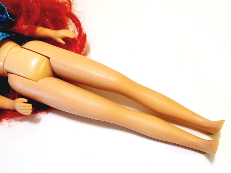 May include: A doll with long red hair and a blue and white dress. The doll's legs are bent at the knees and the feet are pointing towards the camera.