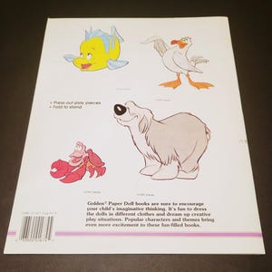 Pode incluir: Contra capa de um livro Golden Paper Doll com ilustra&ccedil;&otilde;es de personagens de desenhos animados. Inclui um peixe amarelo, uma gaivota branca, um caranguejo vermelho e um c&atilde;o cinzento. O texto diz "Press out play pieces. Fold to stand."