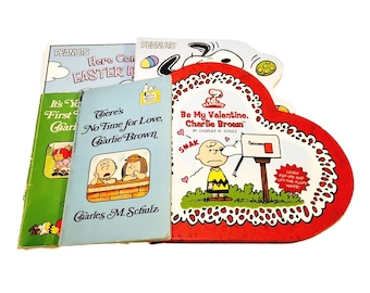 May include: A collection of four Peanuts books, including "It's Your First Christmas, Charlie Brown", "There's No Time for Love, Charlie Brown", "Be My Valentine, Charlie Brown", and "Here Comes Easter, Charlie Brown".
