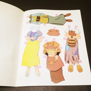 May include: A page from a children's paper doll book featuring illustrations of various outfits. The outfits include a yellow dress, a green and brown outfit, and a brown dress with an apron. The illustrations are colorful and whimsical.