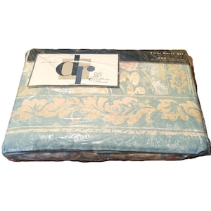 May include: A Twin Sheet Set, wrapped in clear plastic. The sheets have a light blue background with a floral pattern in beige and other colors. The packaging includes a label with the text "dr" and "100% Cotton".
