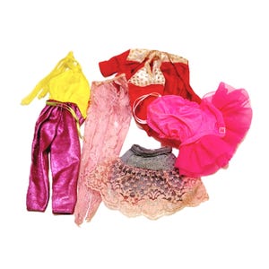 May include: A set of five doll clothes, including a pink and white lace skirt, a pink tulle skirt, a pink and white lace top, a red top with a gold trim, and a purple velvet pantsuit.