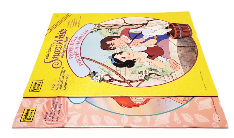 May include: Two vintage Golden Books paper doll sets. The top set features Snow White and the Seven Dwarfs, with a yellow background and illustrations of the characters. The bottom set has a pink background with an illustration of a mermaid.