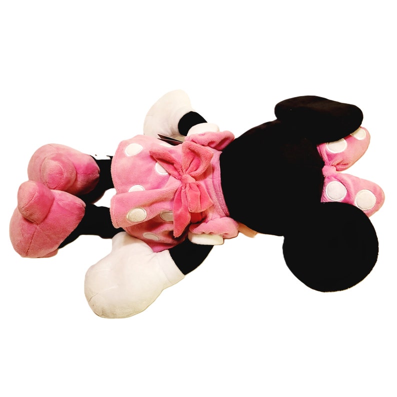 May include: A pink plush Minnie Mouse toy with white polka dots and a pink bow. The toy is lying on its back with its arms and legs outstretched.
