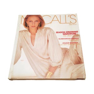 May include: A vintage McCall's magazine from January featuring a cover image of a person wearing a cream-colored, long-sleeved, textured blouse. The cover text includes 'SEASON-SPANNING WARDROBE', 'GLAMOUROUS EVENINGS', and 'HOLIDAY BOUTIQUE'.