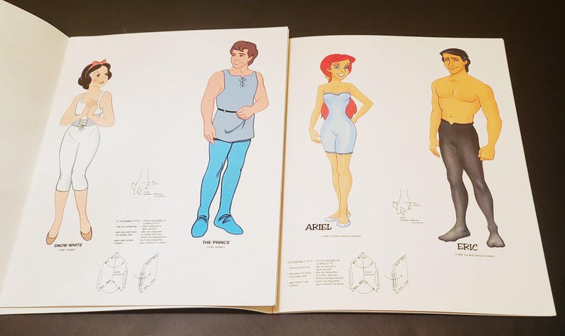 May include: Open book featuring illustrations of Disney characters Snow White, The Prince, Ariel, and Eric. Each character is depicted in a unique outfit with accompanying text labels.
