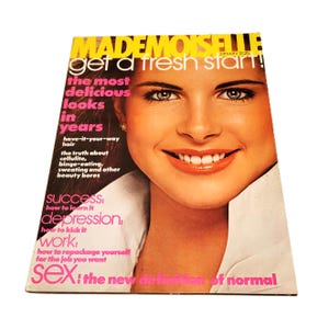 May include: A vintage Mademoiselle magazine cover featuring a smiling woman with fair skin. The cover has text in yellow, pink, and white, including "get a fresh start!" and "the most delicious looks in years." The magazine is from January.