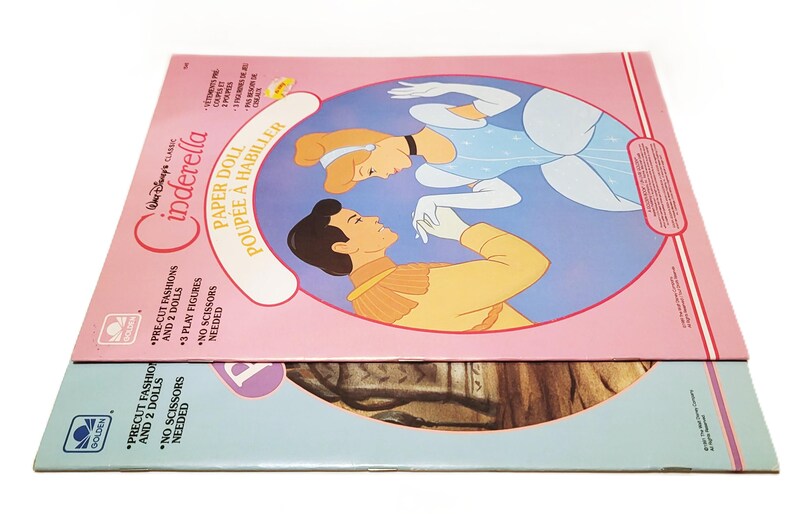 Pode incluir: Conjunto de bonecas de papel Cinderela da Disney vintage. A caixa rosa apresenta Cinderela e o Pr&iacute;ncipe Encantado, com o texto "PAPER DOLL POUPEE A HABILLER". O conjunto inclui modas pr&eacute;-cortadas, 2 bonecas e 3 figuras de jogo. A caixa inferior &eacute; azul e castanha.