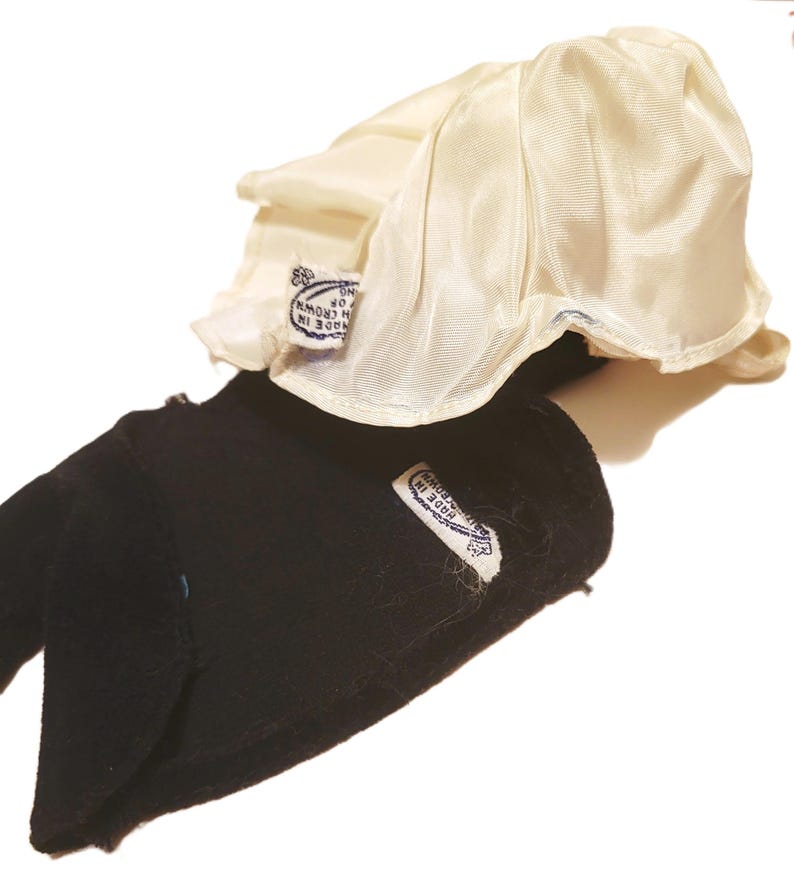 May include: A black velvet hat with a cream-colored satin lining. The hat has a rounded crown and a brim that curves upwards. A small tag is sewn on the hat with text that reads "MADE IN CROWN".
