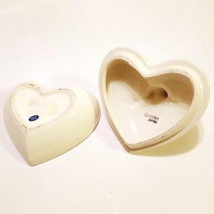 May include: White ceramic heart-shaped trinket box with a lid. The lid has the text "&copy;DISNEY JAPAN" on the bottom. The bottom of the box has a blue sticker that says "MADE IN JAPAN".