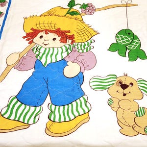 May include: A vintage quilt featuring a red-haired girl with a straw hat, wearing overalls and holding a stick. She is accompanied by a brown and white dog with green striped ears. The quilt has a white background with a blue and white checkered border and a row of purple berries.