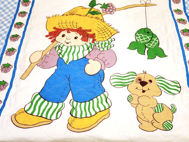 May include: A vintage quilt featuring a red-haired girl with a straw hat, wearing overalls and holding a stick. She is accompanied by a brown and white dog with green striped ears. The quilt has a white background with a blue and white checkered border and a row of purple berries.
