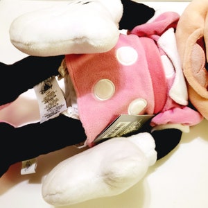May include: Pink plush Minnie Mouse toy with white polka dots, black shoes, and a white bow. The toy has a white tag with the Disney logo and text.