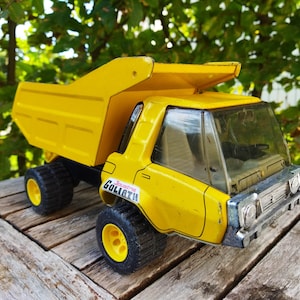 May include: Yellow toy dump truck with a black bed and black tires. The truck has a clear plastic windshield and a sticker that says "Goliath" on the side.