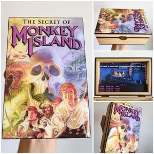 May include: Wooden box featuring the cover art of "The Secret of Monkey Island" video game. The artwork includes a skull, pirates, and the game's title. The box has a hinged lid and a clasp.