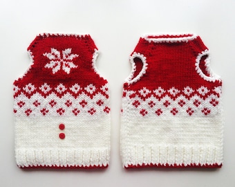 May include: Two sleeveless knitted sweaters in red and white. The top section is solid red with a white snowflake pattern, followed by a red and white diamond motif. The bottom section is solid white with a ribbed hem and two red buttons.
