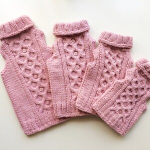 May include: Four pink knitted sweaters with a cable knit pattern and button closures. The sweaters are arranged in a row, with the largest sweater at the top and the smallest sweater at the bottom.