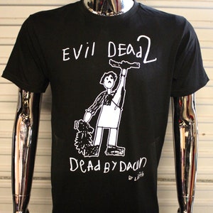 Puede incluir: Camiseta negra con un gráfico blanco de un personaje de palo sosteniendo una motosierra y el texto "Evil Dead 2 Dead By Dawn by Lith".