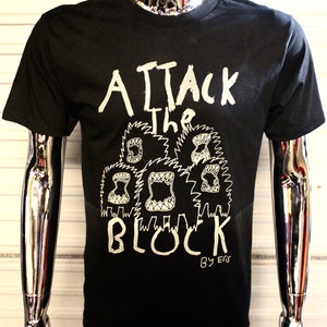 May include: Black t-shirt with a white graphic print of a group of cartoon monsters with the text "Attack the Block" and "By Ers" below.