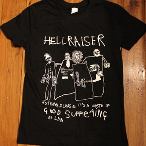 May include: Black t-shirt with a white graphic of a band called "Hellraiser". The graphic features stick figures of the band members and the text "No tears please, it's a waste of good suffering by Lima".