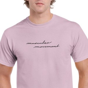 May include: A light pink t-shirt with the text "muscular movement" written in black cursive script.