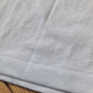 May include: Close-up of the white fabric hem of a garment, showing the stitching detail.