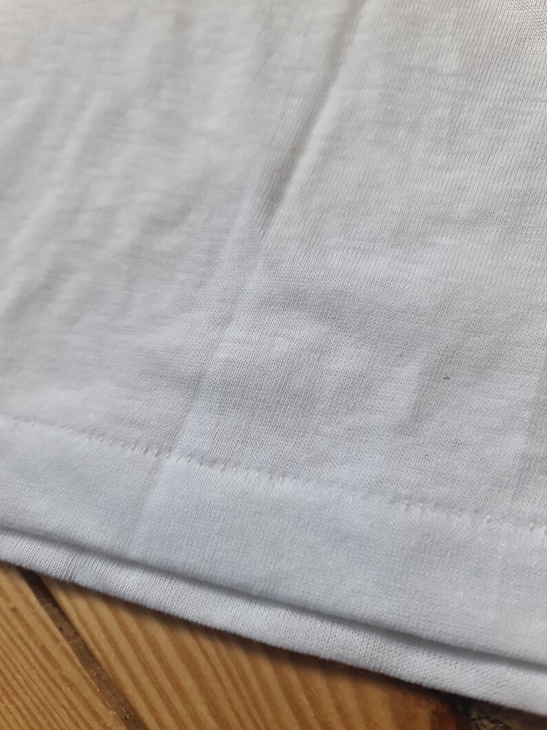 May include: Close-up of the white fabric hem of a garment, showing the stitching detail.