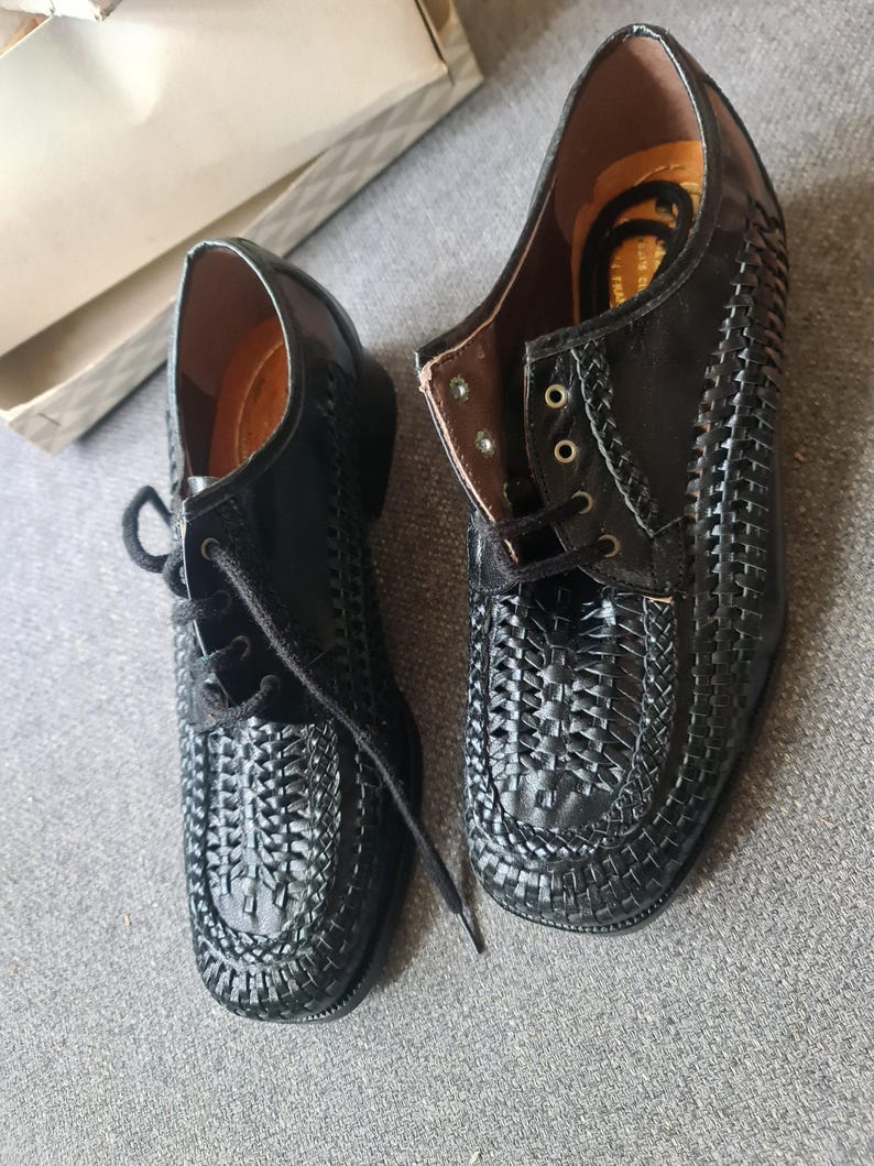 May include: A pair of black leather shoes with a woven design. The shoes have laces and a rounded toe.