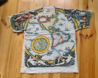 May include: White t-shirt with a vintage world map print. The map is in blue, yellow, and red colors and features the continents of North and South America. The words "PACIFICA" and "ATLANTICA" are visible on the map.