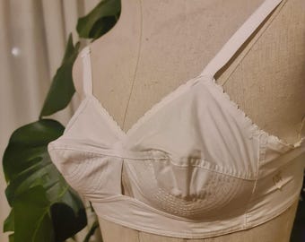 Puede incluir: Sujetador blanco de estilo vintage con tirantes ajustables y un detalle de ojo de cerradura. El sujetador presenta un diseño clásico con detalles de costura en las copas y un borde festoneado.