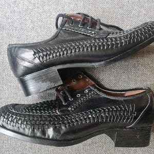 May include: A pair of black leather shoes with a woven pattern. The shoes have a lace-up closure and a low heel.