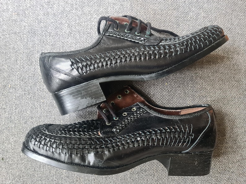 May include: A pair of black leather shoes with a woven pattern. The shoes have a lace-up closure and a low heel.