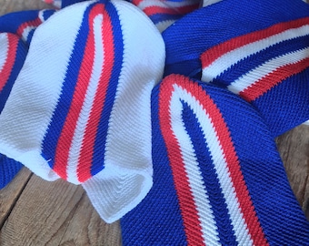Puede incluir: Una pila de gorros de punto a rayas azules, blancas y rojas. Los gorros están hechos de un hilo suave y texturizado.