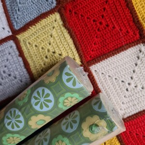 Puede incluir: Dos rollos de papel pintado vintage con fondo verde y un estampado floral repetitivo en azul claro y amarillo. Los rollos est&aacute;n parcialmente desenrollados, revelando el dise&ntilde;o. El fondo es un edred&oacute;n de retazos colorido.