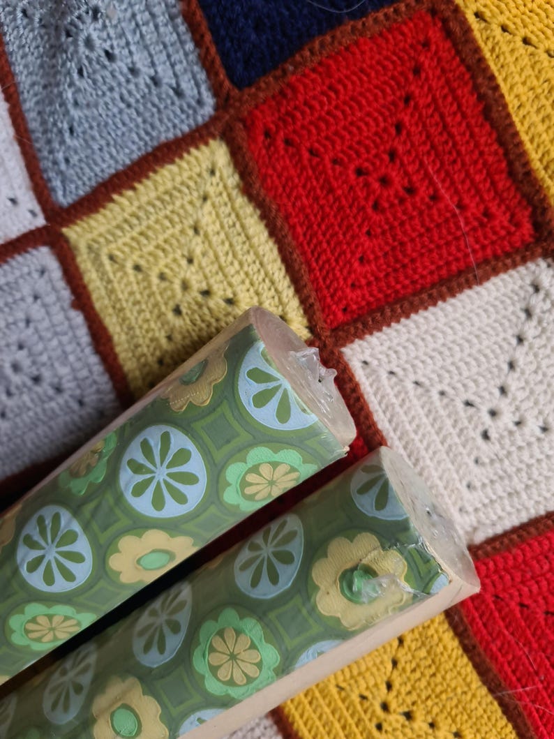 Puede incluir: Dos rollos de papel pintado vintage con fondo verde y un estampado floral repetitivo en azul claro y amarillo. Los rollos est&aacute;n parcialmente desenrollados, revelando el dise&ntilde;o. El fondo es un edred&oacute;n de retazos colorido.