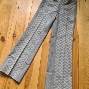 May include: Grey trousers with a geometric pattern. The trousers have a straight leg and a mid-rise waist.